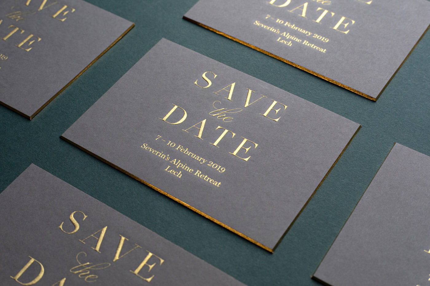 a luxurious chunky grey invitation with gold gilded edges and a gold engraved logo saying Save The Date