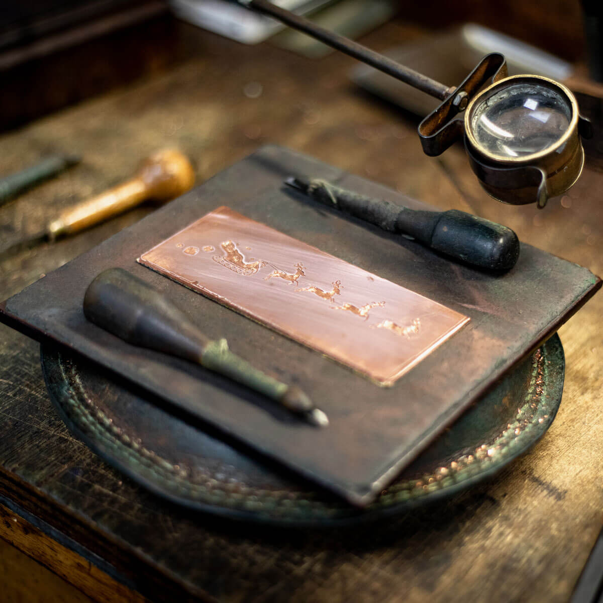 a hand engraved copper plate with a christmas design with tools on a work bench at the wren press